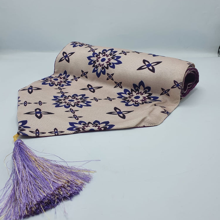 Folded cream and blue floral table runner with its tassel visible.