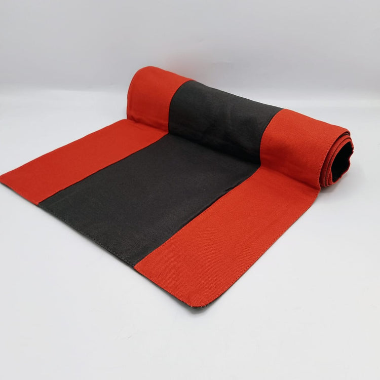 Red and black table runner partly rolled out on a white background.