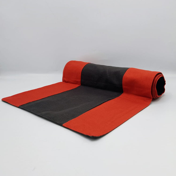 Angled view of a red and black table runner partly rolled out on a white background.