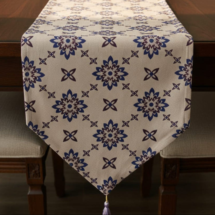 Cream table runner with blue ornamental floral motifs and a tasselled point.