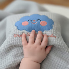 Gray textured blanket with a blue cloud design and a child's hand touching it