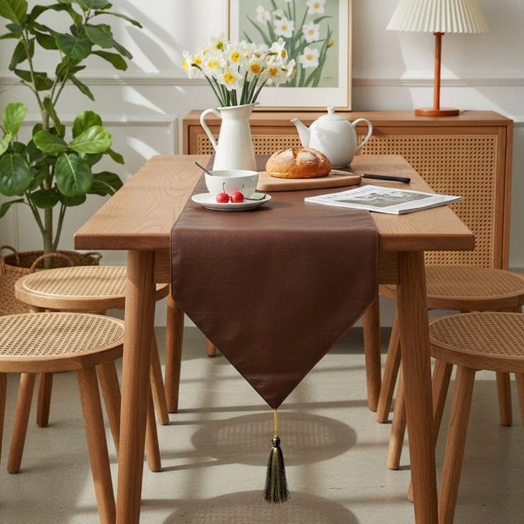 Plain brown table runner with a pointed tasselled end on a dining table.