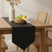Plain black table runner with a pointed end on a wooden dining table.