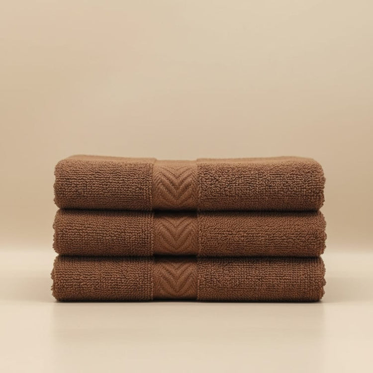 Three folded brown cotton hand towels stacked together.