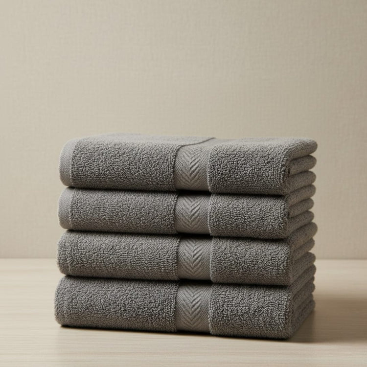 Four folded charcoal grey cotton hand towels stacked together.