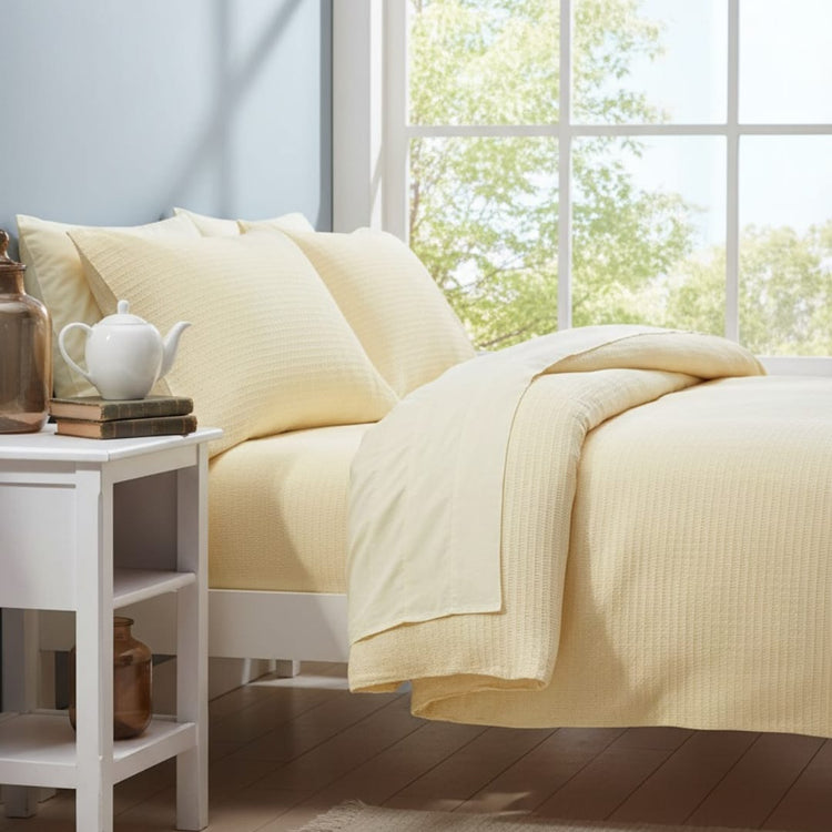 Pale yellow textured blanket draped across a bed with matching pillow covers.