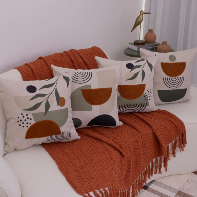 Four cream cushion covers with earthy abstract shapes and black botanical details on a sofa.