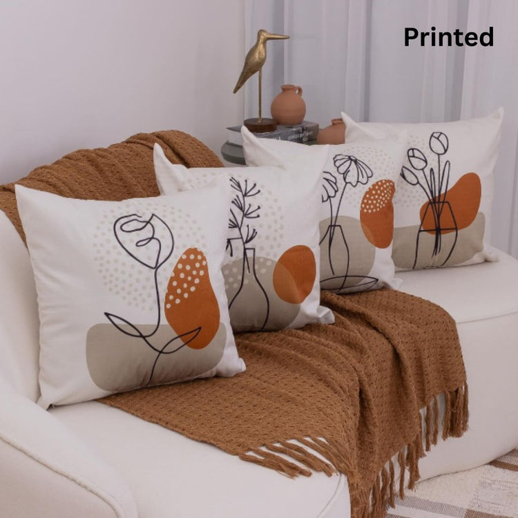 Four cream cushion covers with delicate botanical outlines and orange shapes on a sofa.