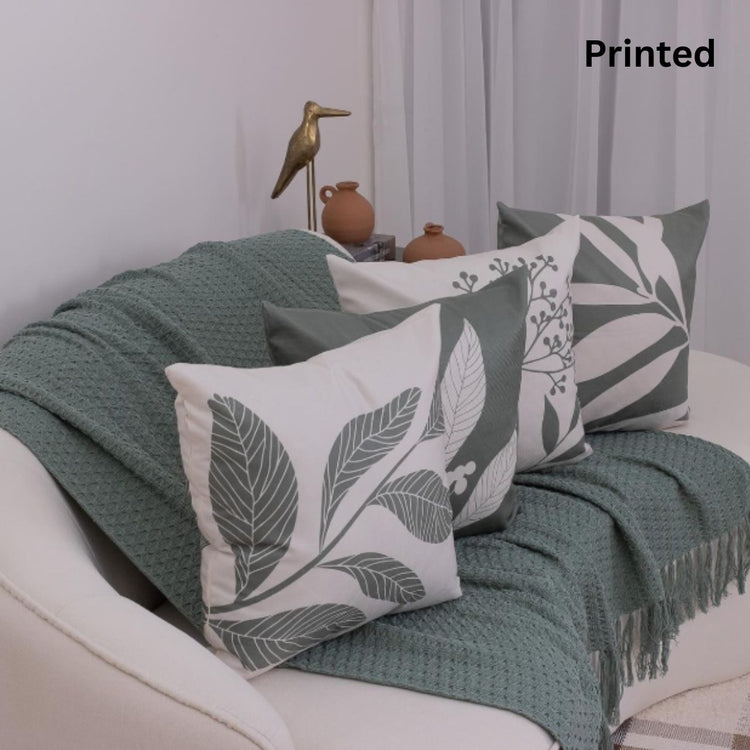 Four white cushion covers with large sage green leaf prints on a sofa.