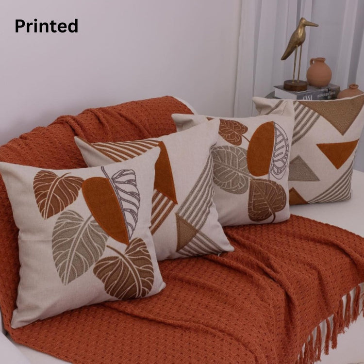 Four cream cushion covers with rust botanical and geometric prints on a sofa.