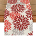 Cream table runner with red and grey floral motifs.