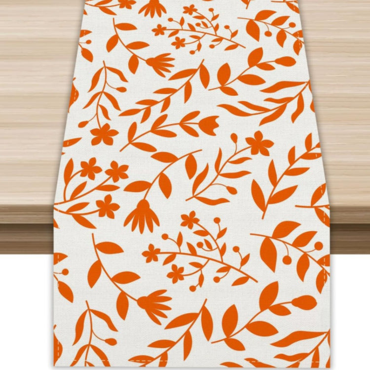 White table runner with orange flowers and leafy branches.