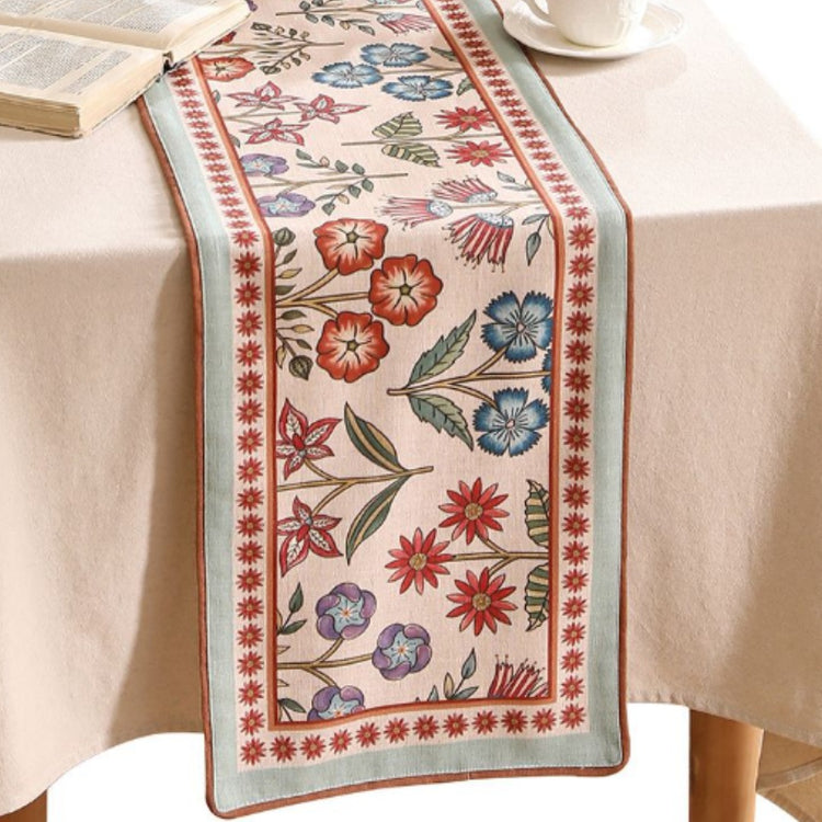 Cream table runner with colourful floral vines and red patterned borders.