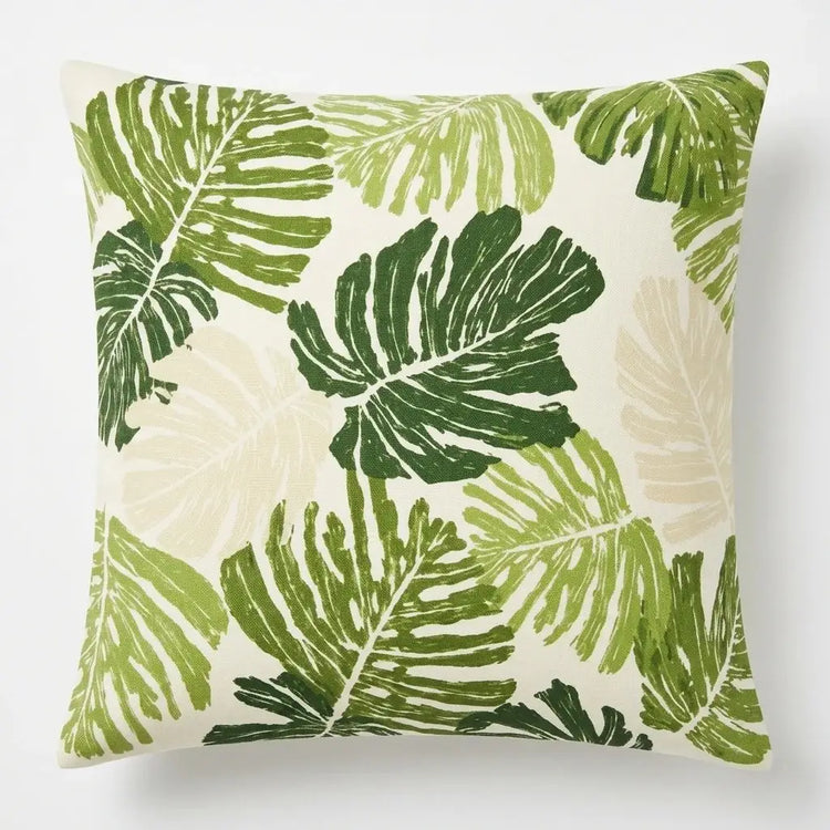Cream cushion cover with scattered light and dark green monstera leaves.