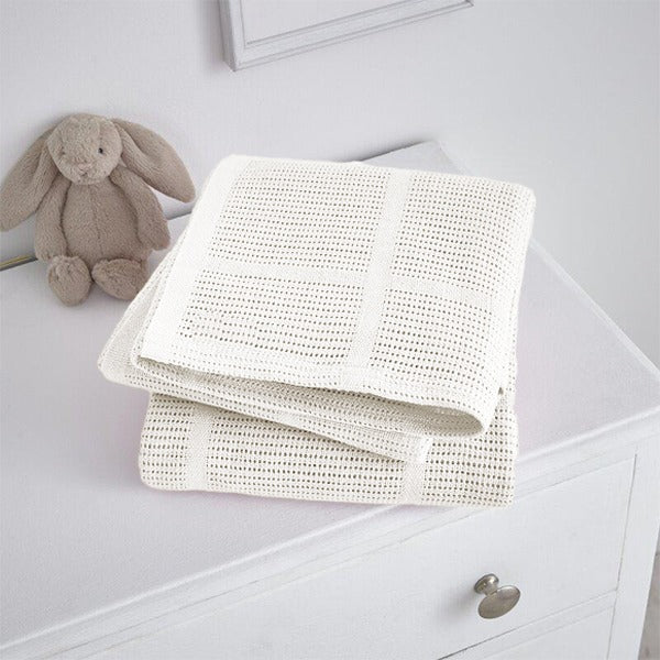 Folded white cellular blanket on a white cabinet beside a plush rabbit.