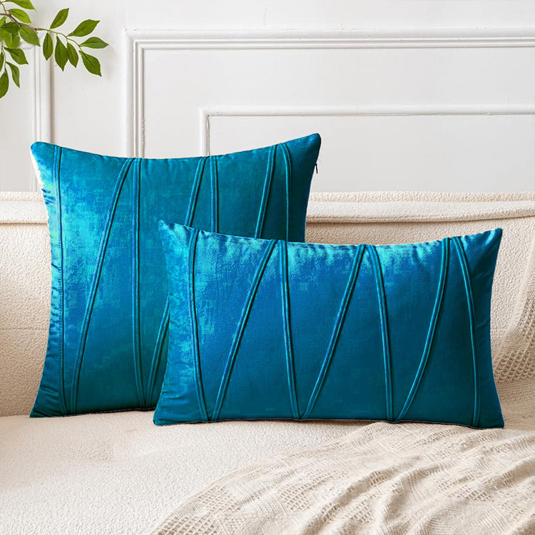 Teal square and rectangular cushion covers with angular stitched lines on a bed.