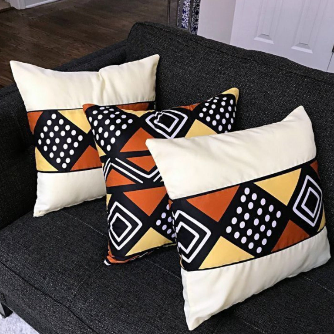 Three cream, black, orange and yellow geometric cushion covers on a dark sofa.
