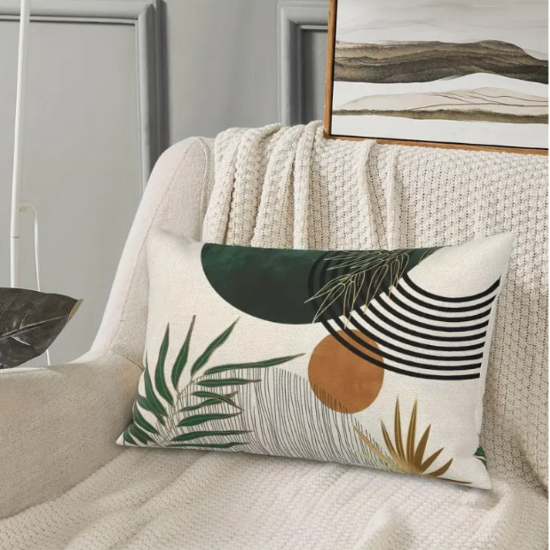 Rectangular cream cushion cover with green leaves, ochre circle and black curved lines on a draped chair