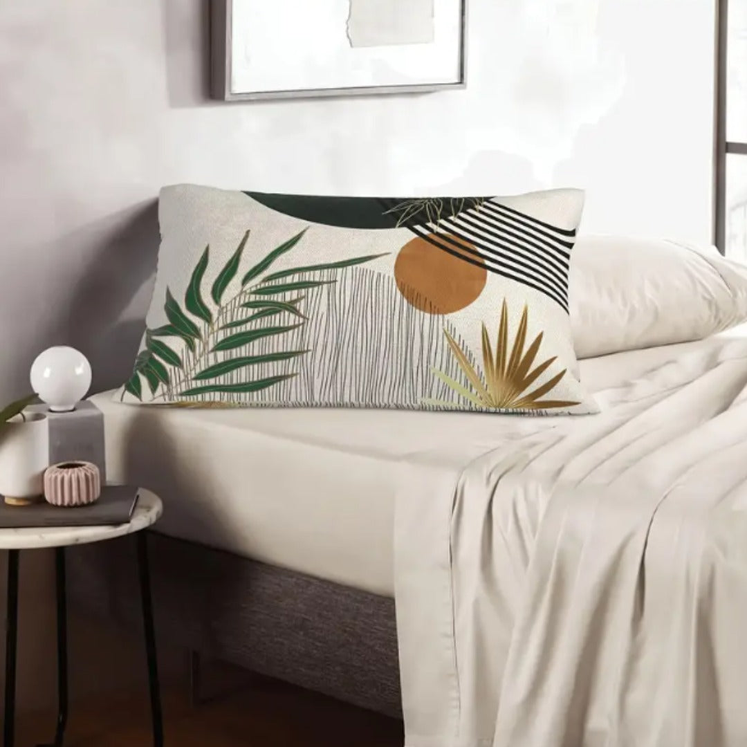 Rectangular cream cushion cover with green leaves and an ochre circle on a pale sofa.