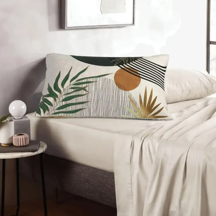 Rectangular cream cushion cover with green leaves and an ochre circle on a pale sofa.
