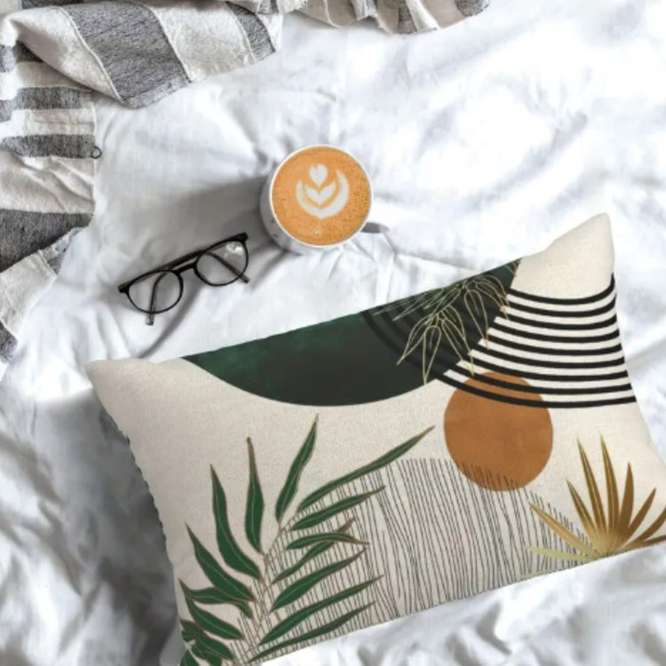 Rectangular botanical cushion cover with green leaves shown on white bedding beside glasses.