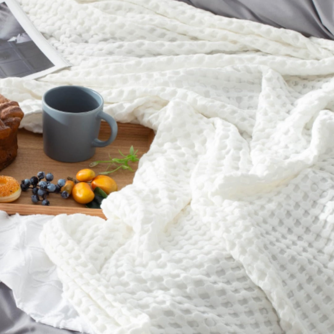 Close-up of white waffle-weave blanket fabric beside a breakfast tray.