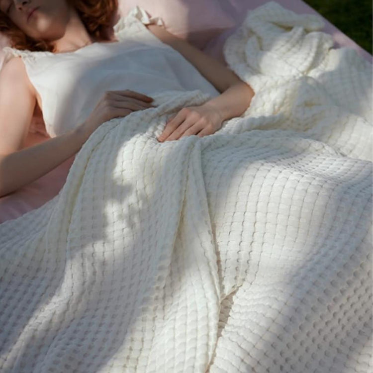 Person resting under a white waffle-weave blanket.