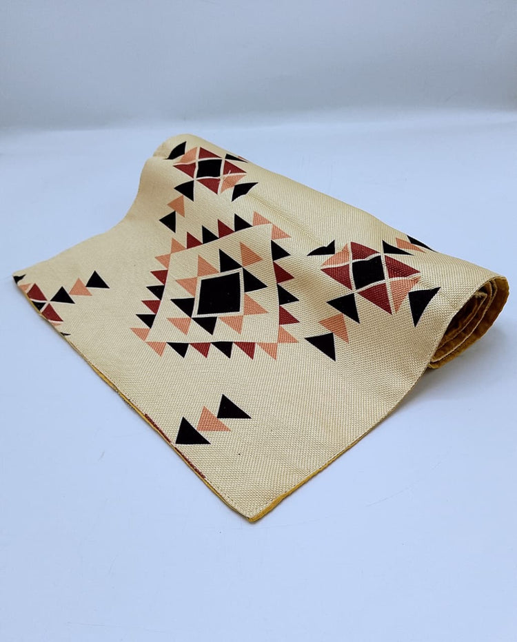 Folded cream table runner with small black, red and beige geometric motifs.