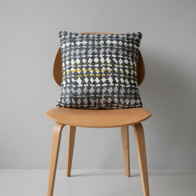 Grey, cream and yellow patterned filled cushion on a wooden chair.