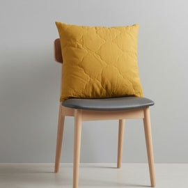 Mustard yellow filled decorative cushion on a wooden chair.
