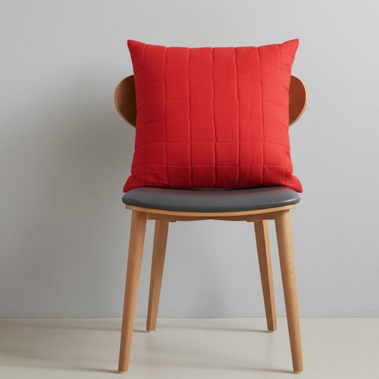 Red filled decorative cushion with stitched lines on a wooden chair.