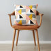 Decorative cushion with pastel geometric triangles on a wooden chair.