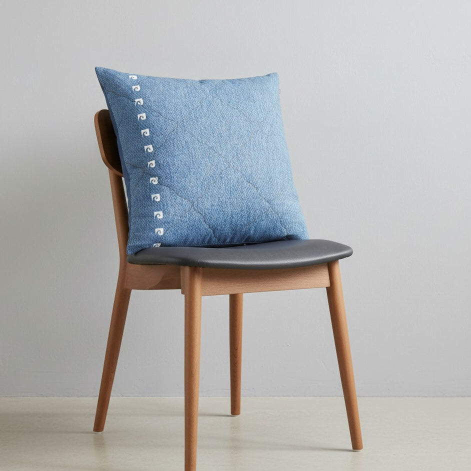 Blue cushion cover with subtle stitched texture displayed on a chair.