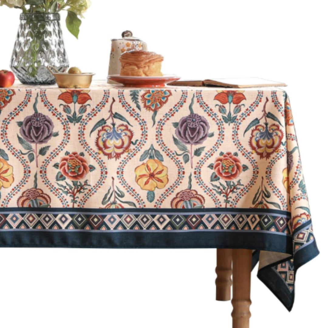 Cream tablecloth with colourful ornamental floral motifs and a dark patterned border.