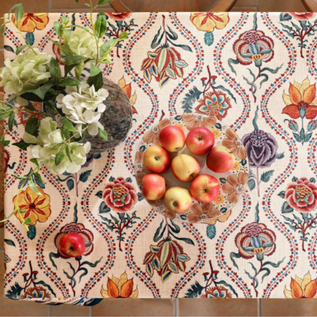 Overhead view of a cream floral tablecloth with colourful scrolling motifs.