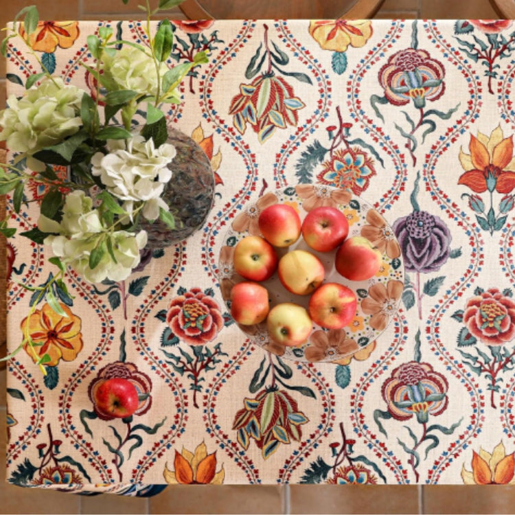 Overhead view of a cream floral tablecloth with colourful scrolling motifs.