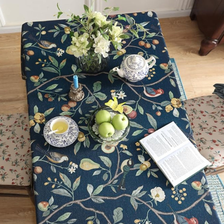 Overhead view of a navy botanical tablecloth beneath fruit, crockery and an open book.