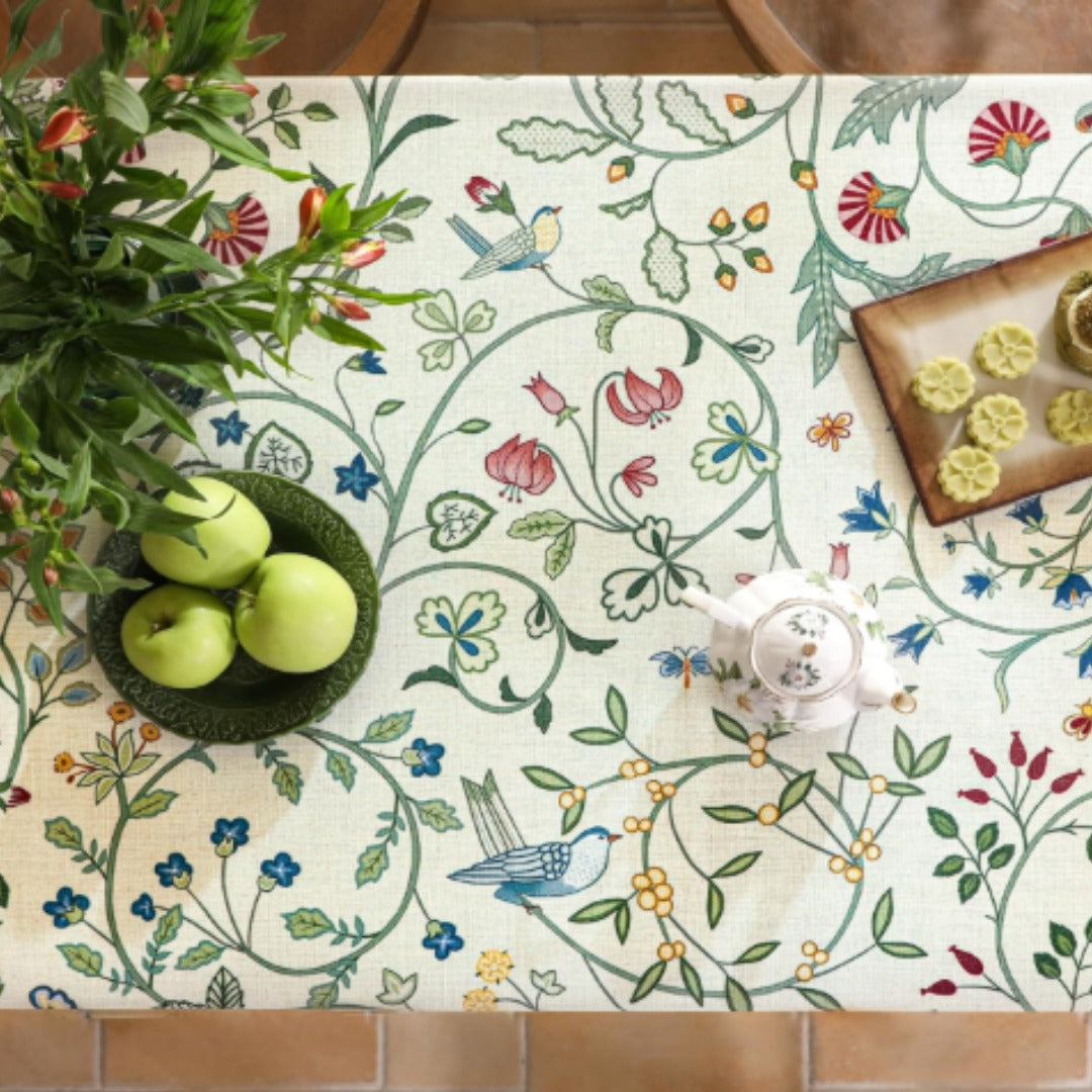 Overhead close view of green leafy vines and small flowers on a cream tablecloth.