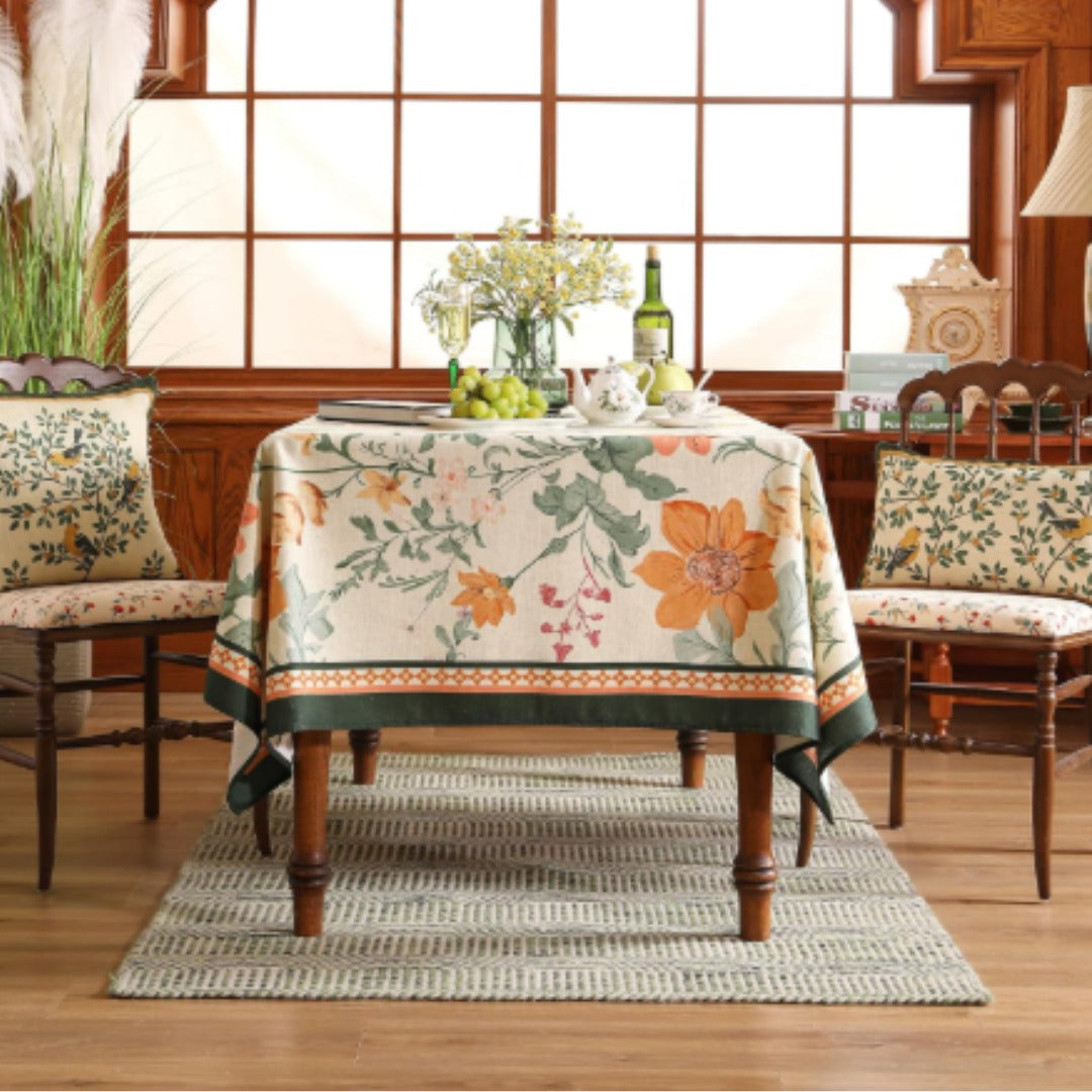 Cream tablecloth with large orange flowers, green leaves and patterned borders.