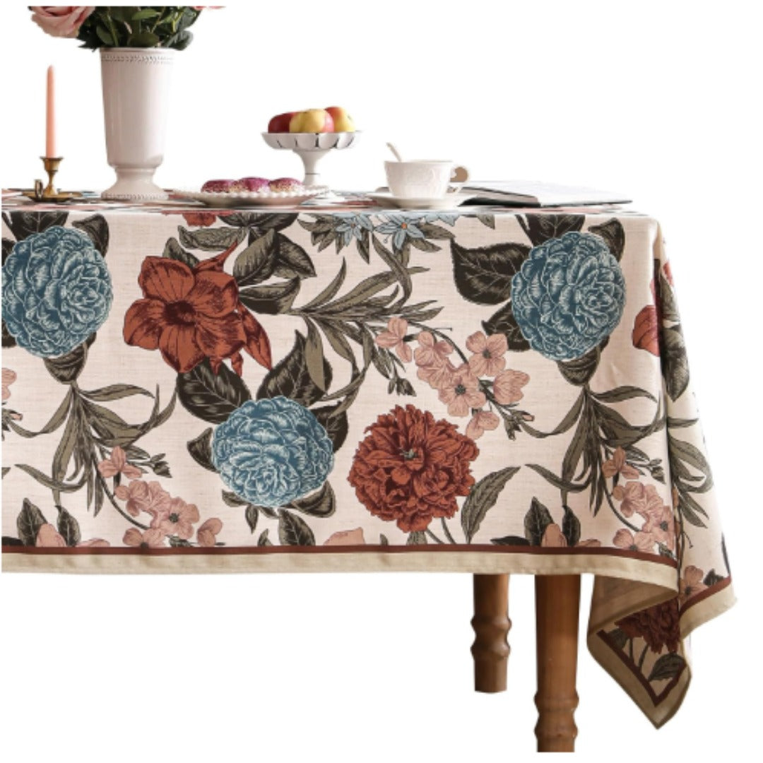 Cream tablecloth with large burgundy and teal flowers and dark leafy stems.