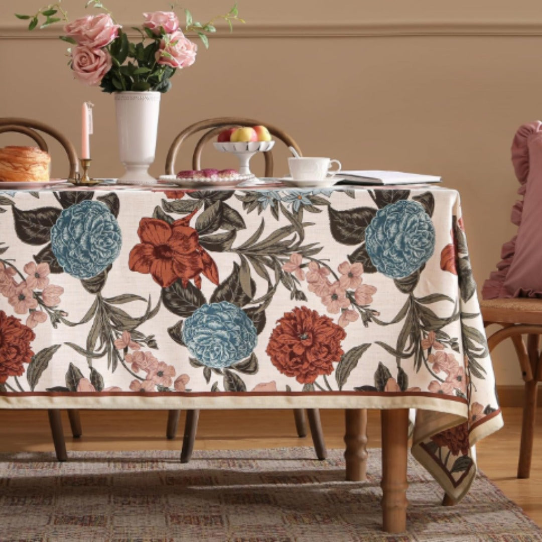 Cream tablecloth with large burgundy and teal flowers and dark leafy stems.