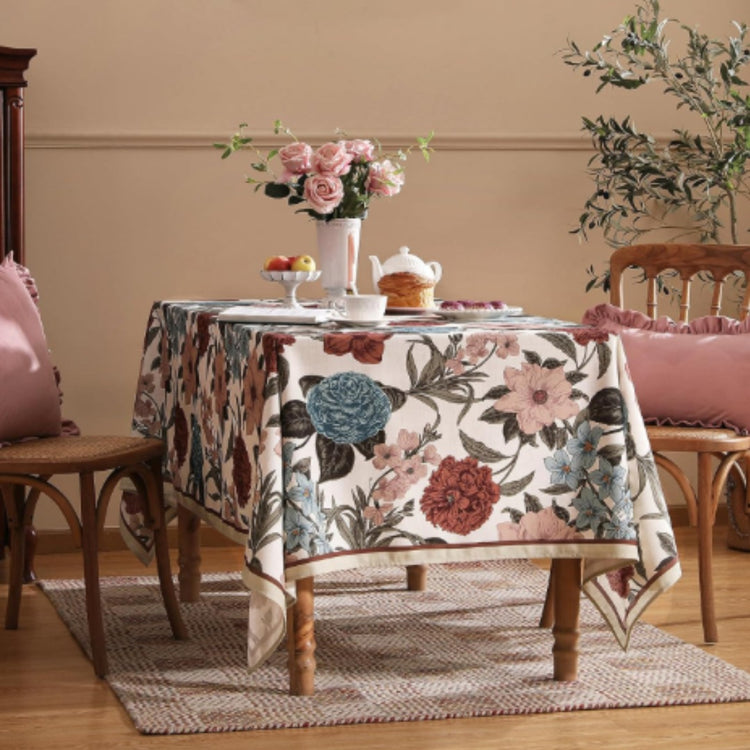 Cream tablecloth with large burgundy and teal flowers and dark leafy stems.
