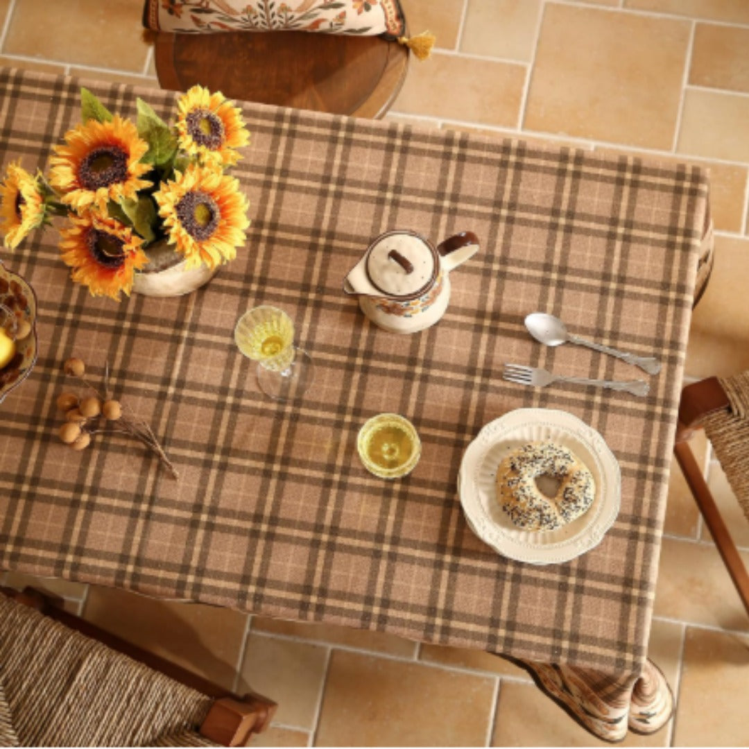 Overhead view of a brown checked tablecloth with cups and sunflowers.