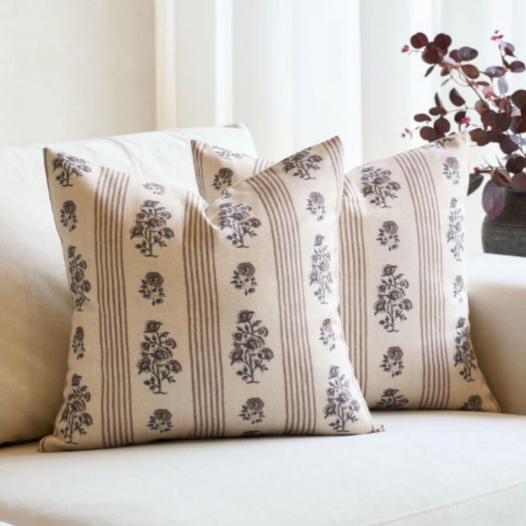 Two cream cushion covers with vertical beige bands and dark botanical motifs.