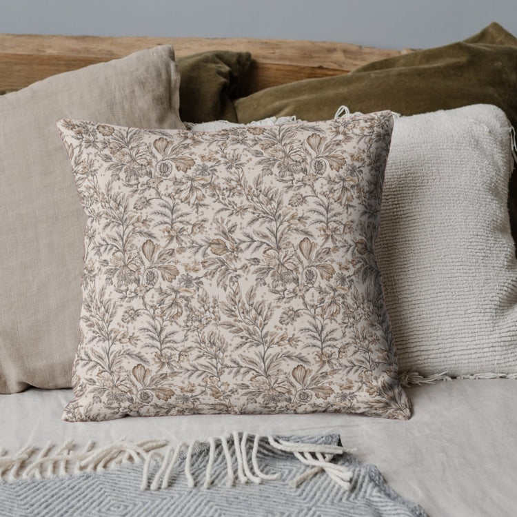 Cream cushion cover with a delicate dense taupe floral pattern on a draped sofa.