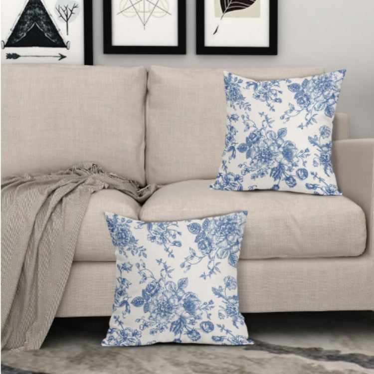 Two white cushion covers with fine blue floral patterns displayed on a sofa and floor.