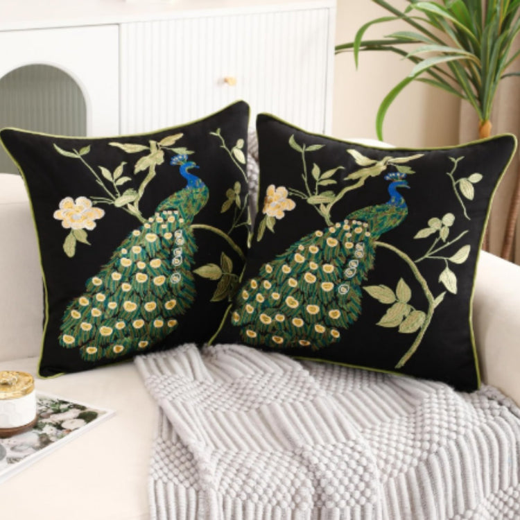 Two black cushion covers with green peacocks and cream flowering branches on a sofa.
