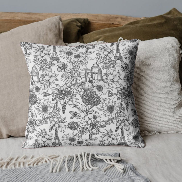 White cushion cover with a dense black botanical pattern on a draped sofa.