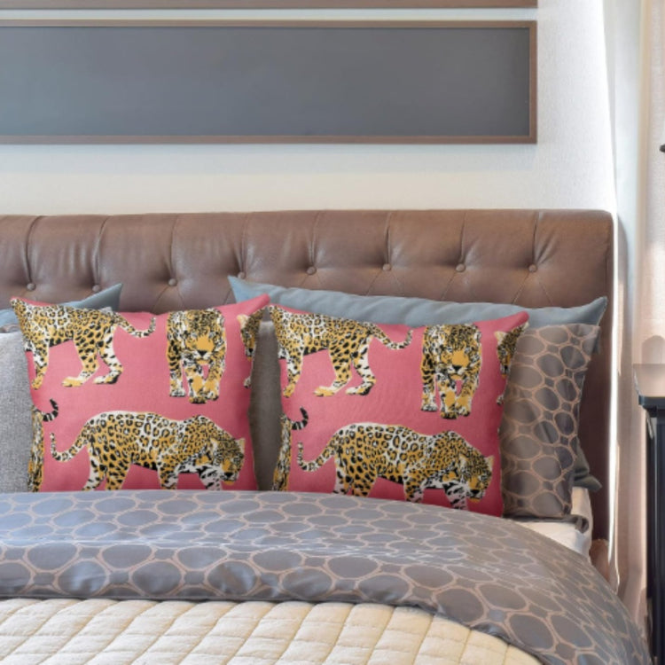 Two pink cushion covers with illustrated spotted big cats on a bed.