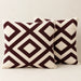 Two cream cushion covers with bold burgundy interlocking diamond patterns on a sofa.